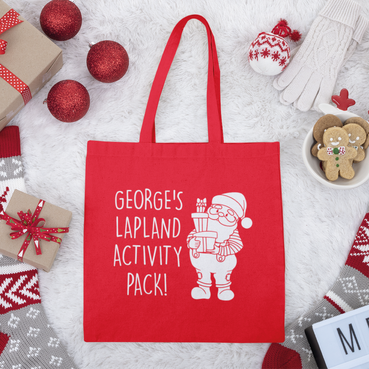 Red tote bag with 'George's Lapland activity pack' written on it with an image of a cartoon santa holding presents