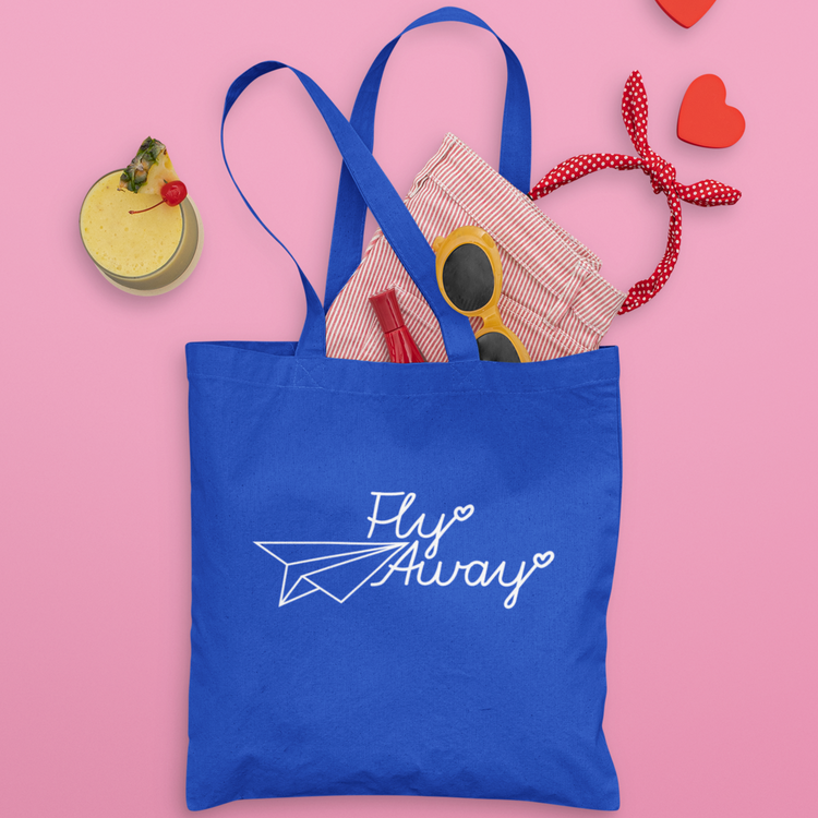 A royal blue tote bag with white text that says 'fly away' written in a calligraphy font with a hear at the end of each word and a line drawing of a paper plane to the left of it