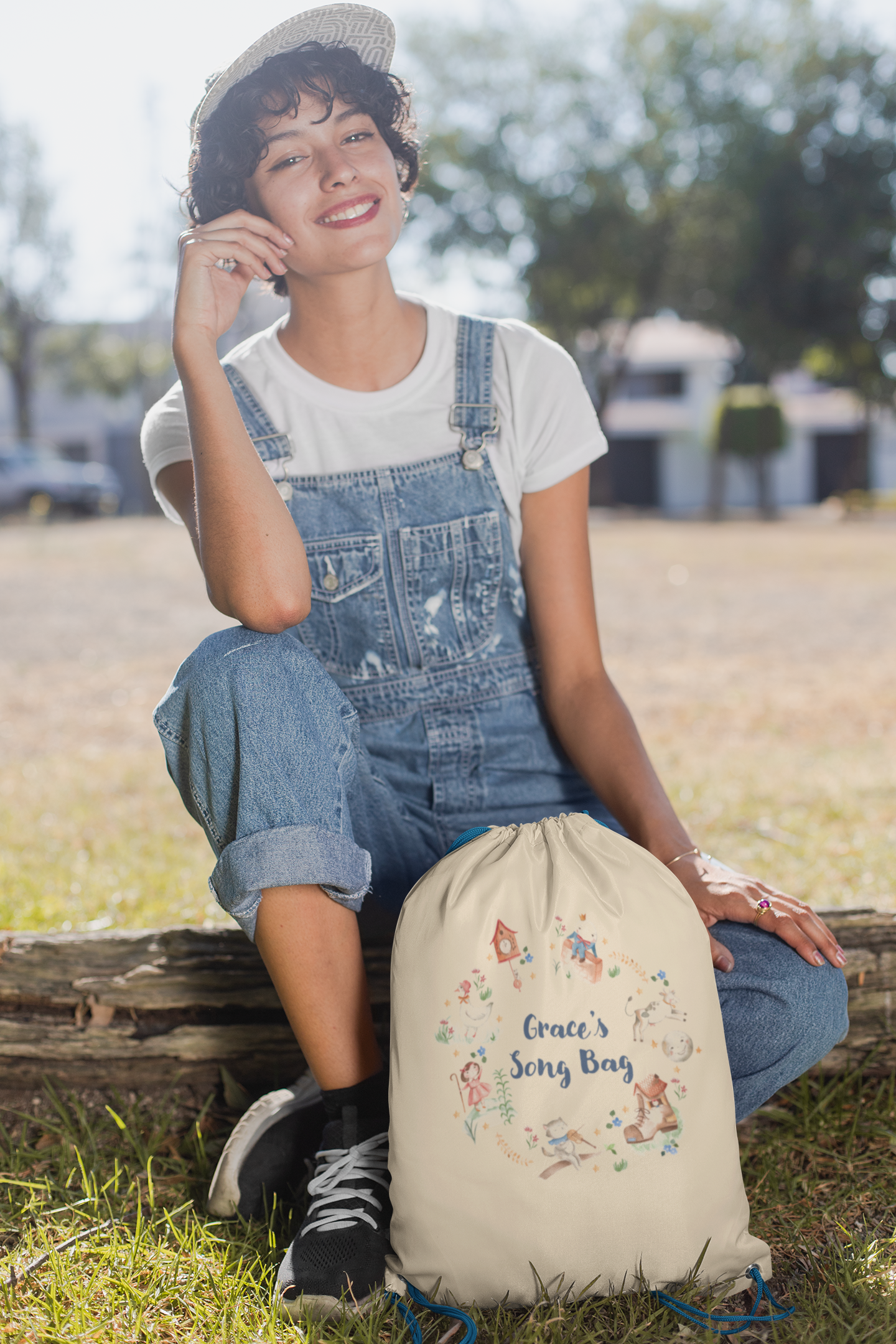 Image of woman holding a cream coloured cotton drawstring bag. Printed on the bag is some colourful illustrations from nursery rhymes, humpty dumpty, little bo peep, a clock, a boot, a goos, a cat and the fiddle and a cow and a moon. The watercolour illustrations are arranged in a wreath shape with the words 'Grace's son bang' written in blue in the middle.