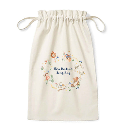 Image shows a cream coloured cotton drawstring pouch / sack. Printed on the bag is some colourful illustrations from nursery rhymes, humpty dumpty, little bo peep, a clock, a boot, a goos, a cat and the fiddle and a cow and a moon. The watercolour illustrations are arranged in a wreath shape with the words 'Grace's son bang' written in blue in the middle.